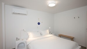 Ett sovrum med en säng, sängbord, ett litet bord, en väggmonterad luftkonditioneringsanläggning, en taklampa och en liten bänk.