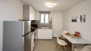 Ett kompakt kök med kylskåp, mikrovågsugn och diskho. Det finns ett matbord med stolar och ett litet fönster ovanför diskhon.