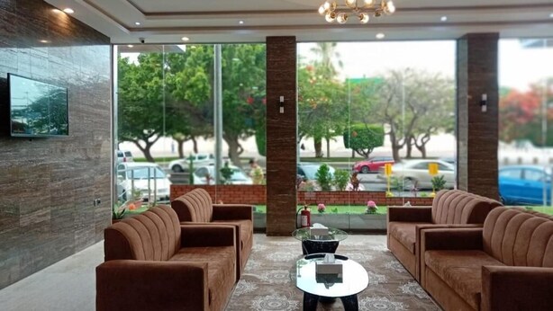 A lobby with a sofa set, a coffee table, and a large window with a view of trees and parked cars. - Nilufer AlHada Hotel (Taif)
