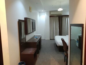 Quarto de hotel com cama, escrivaninha com cadeira, espelho e ar condicionado.