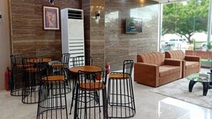 A lobby with a modern design, featuring a seating area with metal chairs and tables, a sofa, and a large air conditioning unit. - Nilufer AlHada Hotel (Taif)