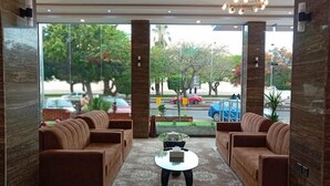 A lobby with a seating area, a coffee table, and large windows offering a view of the street and trees. - Nilufer AlHada Hotel (Taif)