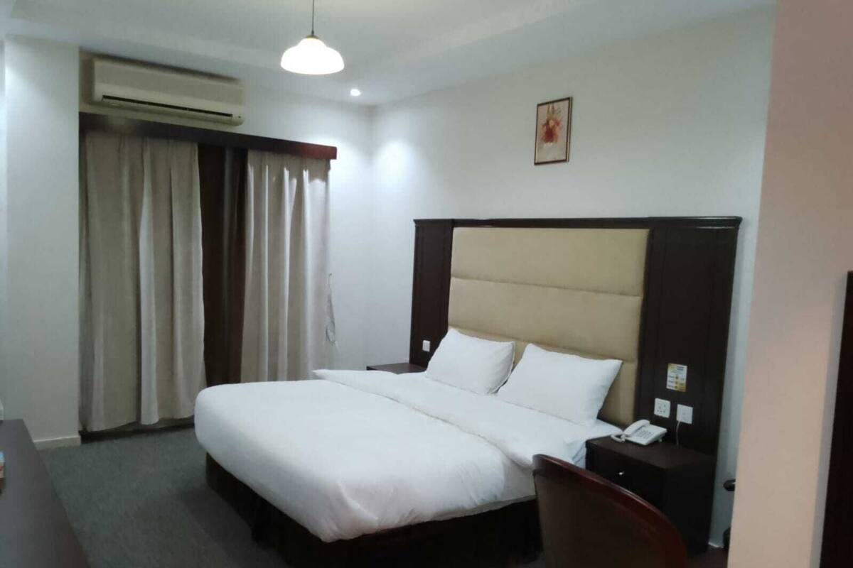 A hotel room with a bed, a desk, a chair, an air conditioning unit, and a telephone.