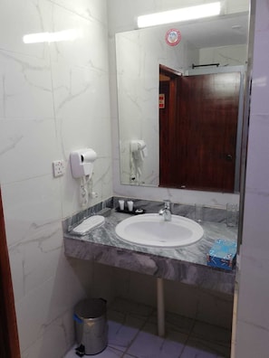 Casa de banho com lavatório de mármore, espelho, secador de cabelo e um cesto de lixo.