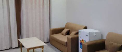 A living room with two sofas, a small table, a refrigerator, and a picture on the wall.