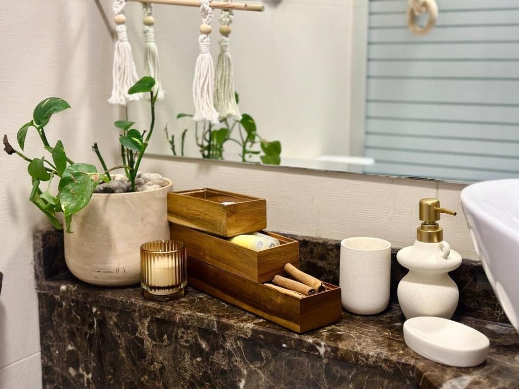Un tocador de baño con encimera de mármol, una planta en maceta, un neceser de madera con artículos de aseo, una vela y un dispensador de jabón.