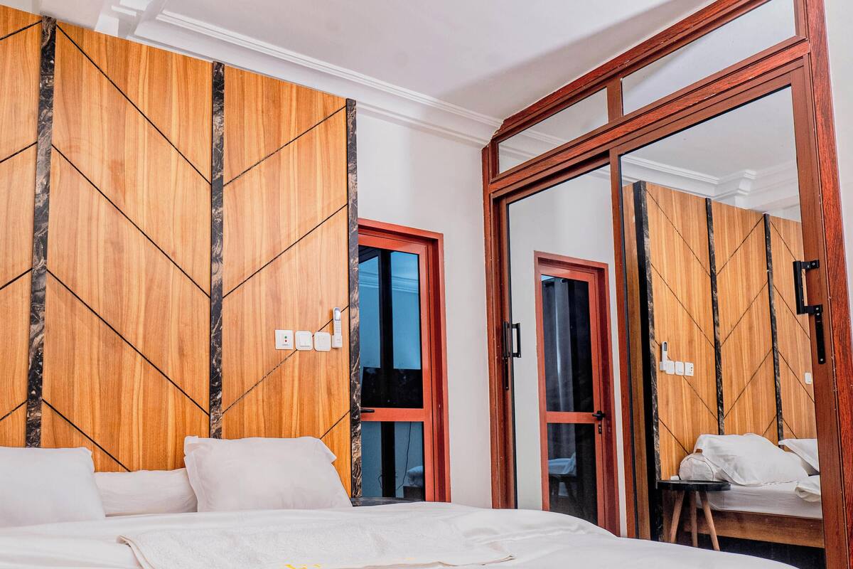 Une chambre d’hôtel avec un lit, un mur recouvert de panneaux de bois et un miroir qui reflète la pièce.