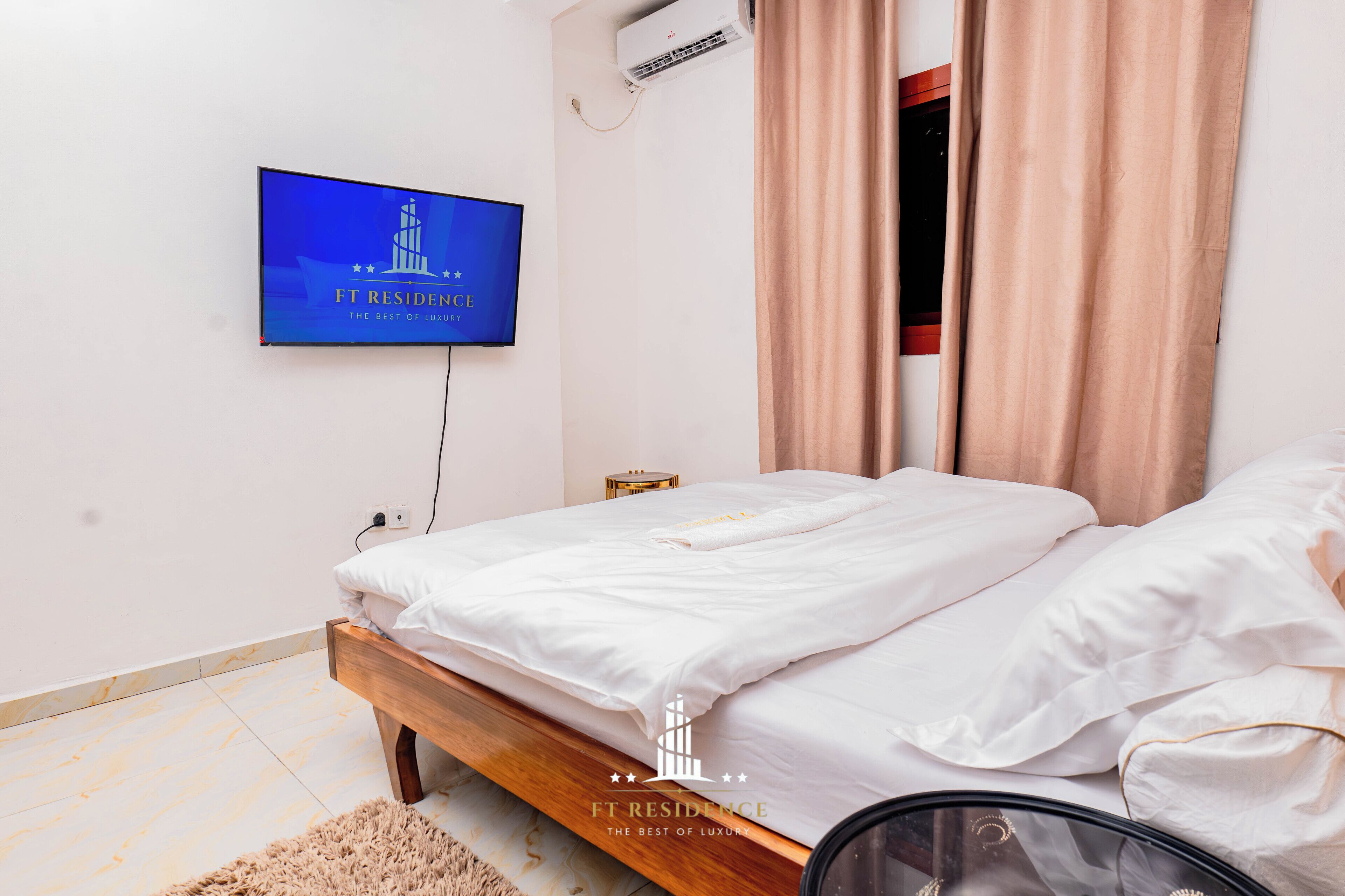 A bedroom with a bed, a TV mounted on the wall, and a window with curtains.