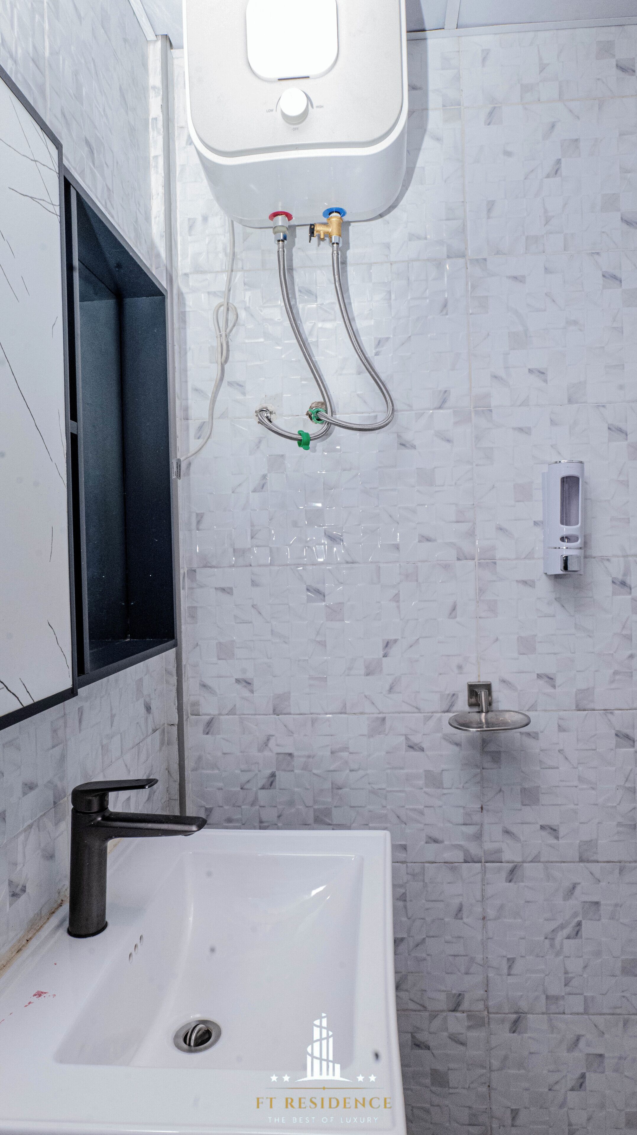 Une salle de bain avec un lavabo blanc, un miroir, une douchette à main et un distributeur de savon fixé au mur.