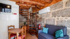 A cozy room with a stone wall, a wooden table with chairs, a blue sofa with teal cushions, and a wooden spiral staircase. - O Palheiro by CVL (Melgaço)