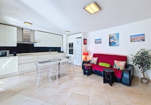 A modern kitchen with white cabinets and a dining area with a clear table and chairs. - N&J - GAMBETTA HORIZON - By sea - Terrace (Niza)