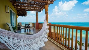 Un balcon avec un hamac, une balustrade en bois et une vue sur l’océan.