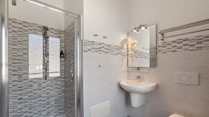 Un baño moderno con cabina de ducha de vidrio, un lavabo blanco y un inodoro.