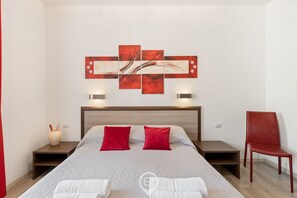 Ein Hotelzimmer mit Bett, einem roten Sessel, einem Nachttisch, einem Wandbild und einer Vase.