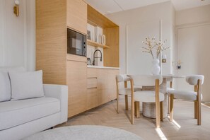 A modern living room with a white sofa, wooden cabinets, a kitchen area with a Bosch refrigerator, and a dining table with chairs. - A Wonderfull 1-Br - Opéra (Paris)