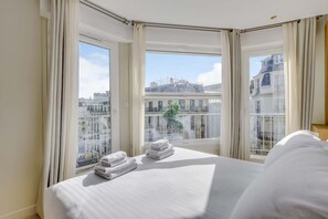 Une chambre d’hôtel avec un grand lit, deux fenêtres avec des rideaux et une vue sur les bâtiments de la ville.
