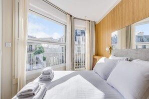 A hotel room with a large bed, a wooden headboard, and a view of the cityscape through large windows. - A Wonderfull 1-Br - Opéra (Paris)