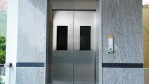 En moderne elevator med metalfinish, placeret i en bygning med granitvægge og flisegulv.
