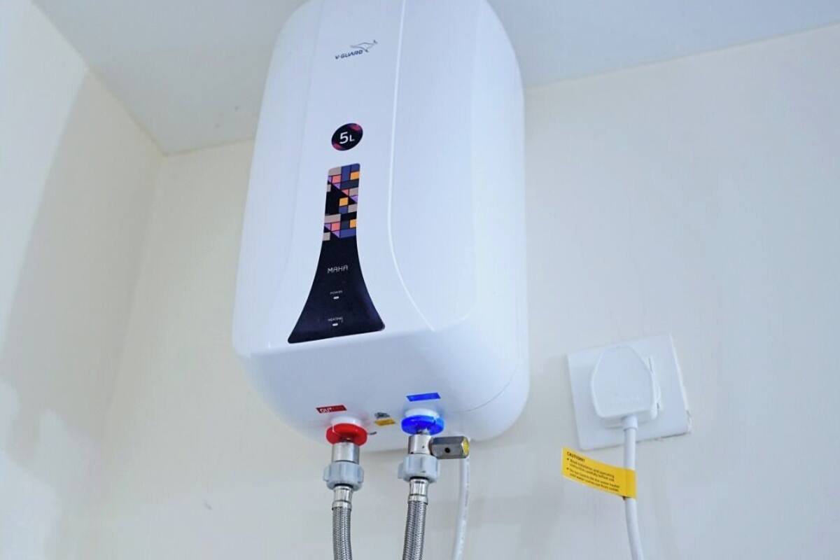 Un chauffe-eau blanc fixé au mur, avec deux tuyaux métalliques qui y sont raccordés et une prise électrique blanche.