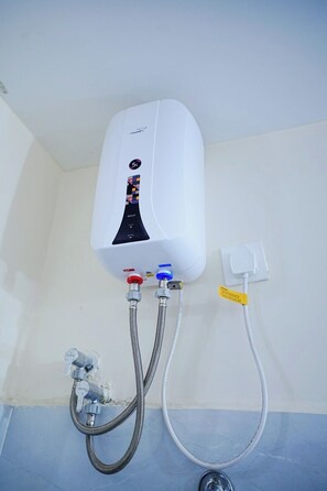 Un chauffe-eau blanc fixé au mur, avec deux tuyaux métalliques qui y sont raccordés et une prise électrique blanche.