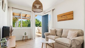 A living room with a sofa, a small table, a hanging light fixture, and a window with a view of greenery.
