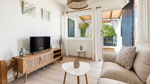 A living room with a TV, a white coffee table, a sofa, a wicker lamp, and a view of the outside.