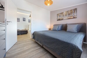 Un dormitorio con cama, armario, puerta a otra habitación y un cuadro en la pared.