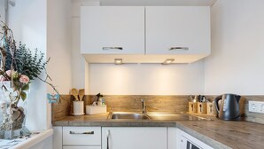 Una cocina moderna con armarios blancos, encimera de madera, pileta de acero inoxidable y lavavajillas.