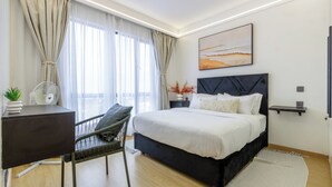 Un dormitori modern amb un llit, un escriptori, una cadira i una finestra gran amb cortines.