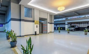 A clean, modern indoor parking area with a clear exit sign, potted plants, and a ceiling light fixture. - Skypiea Loft |City view 1BR in Riara with a Pool close to Westlands and CBD (PQ27+WHX, Riara Rd, Nairobi)
