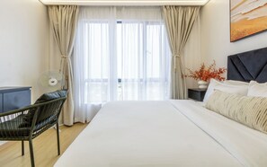 Une chambre d’hôtel avec un grand lit, une chaise, une table de chevet ornée d’un vase de fleurs et un ventilateur fixé au mur.