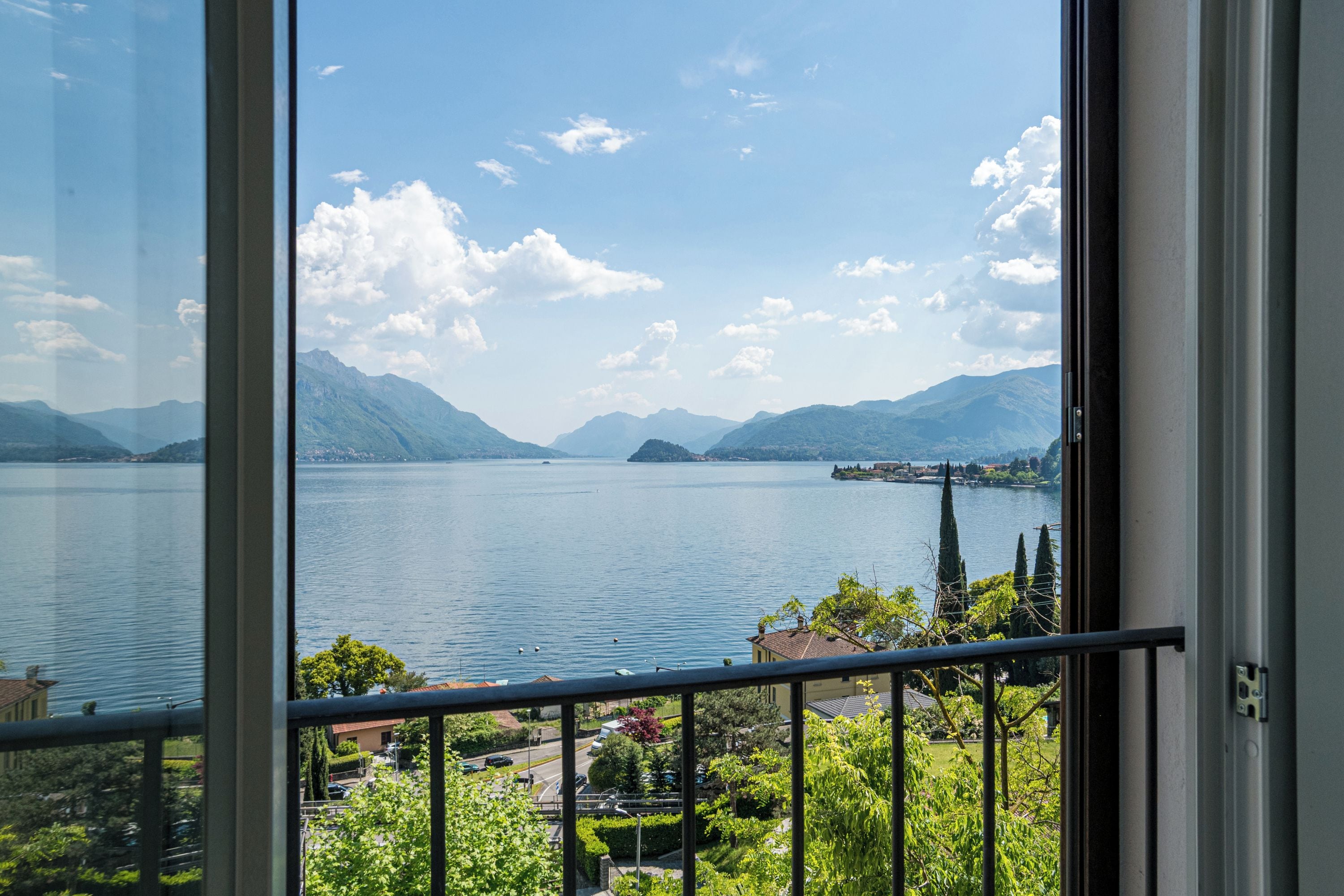 Ein See mit Bergen im Hintergrund, Blick vom Balkon mit Geländer.