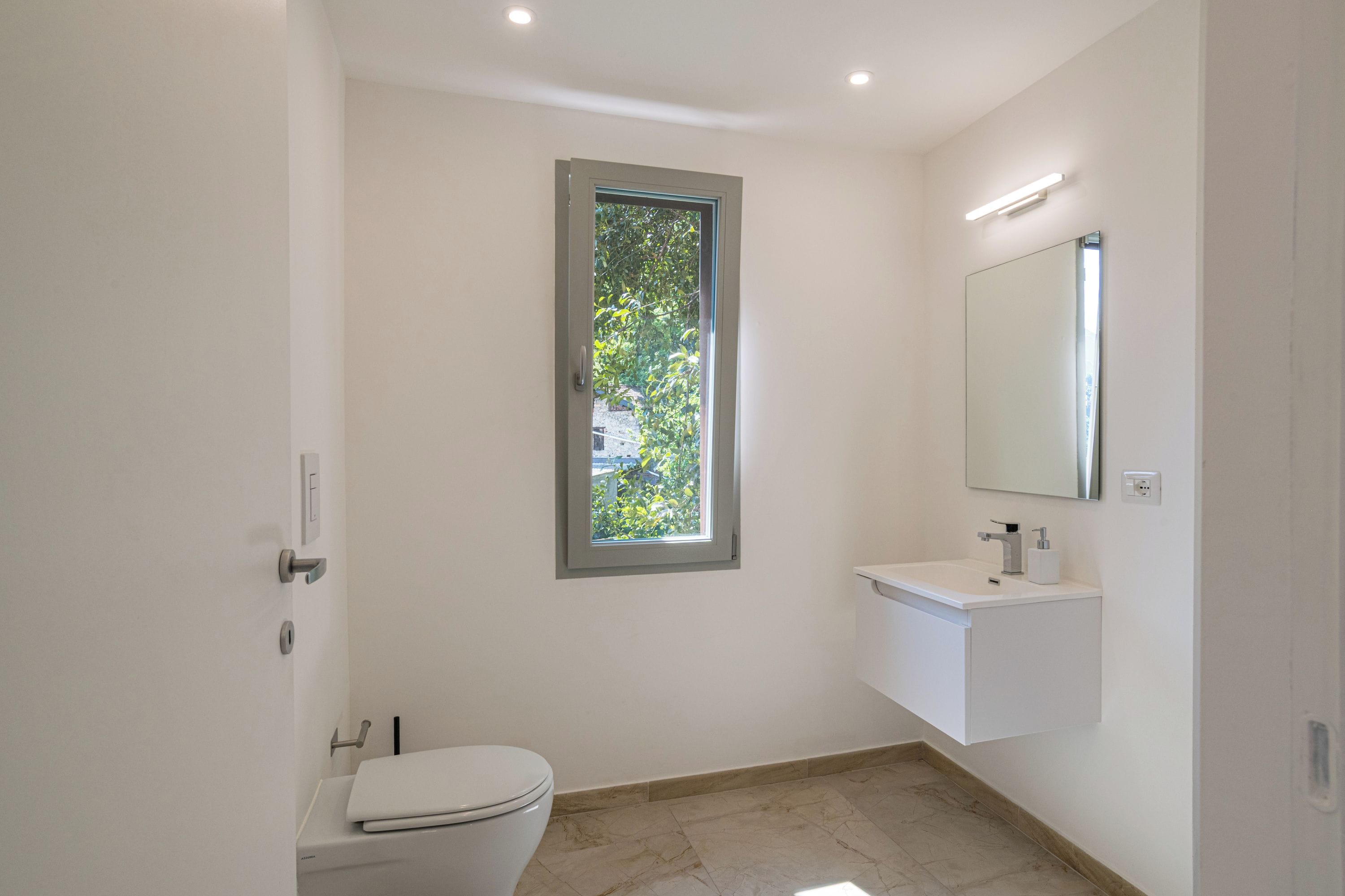 Un bany modern amb un vàter, una finestra, un lavabo i un mirall.