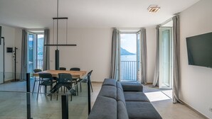 A modern living room with a sofa, dining table, chairs, and a TV. - Sant' Anna Deluxe (Menaggio)