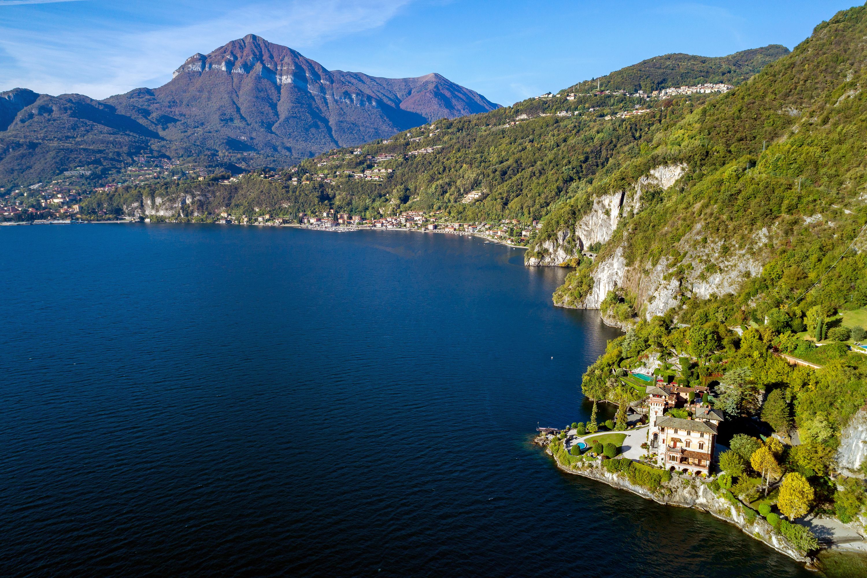 Una proprietà sul lago con una casa grande, circondata da una vegetazione lussureggiante e montagne sullo sfondo.