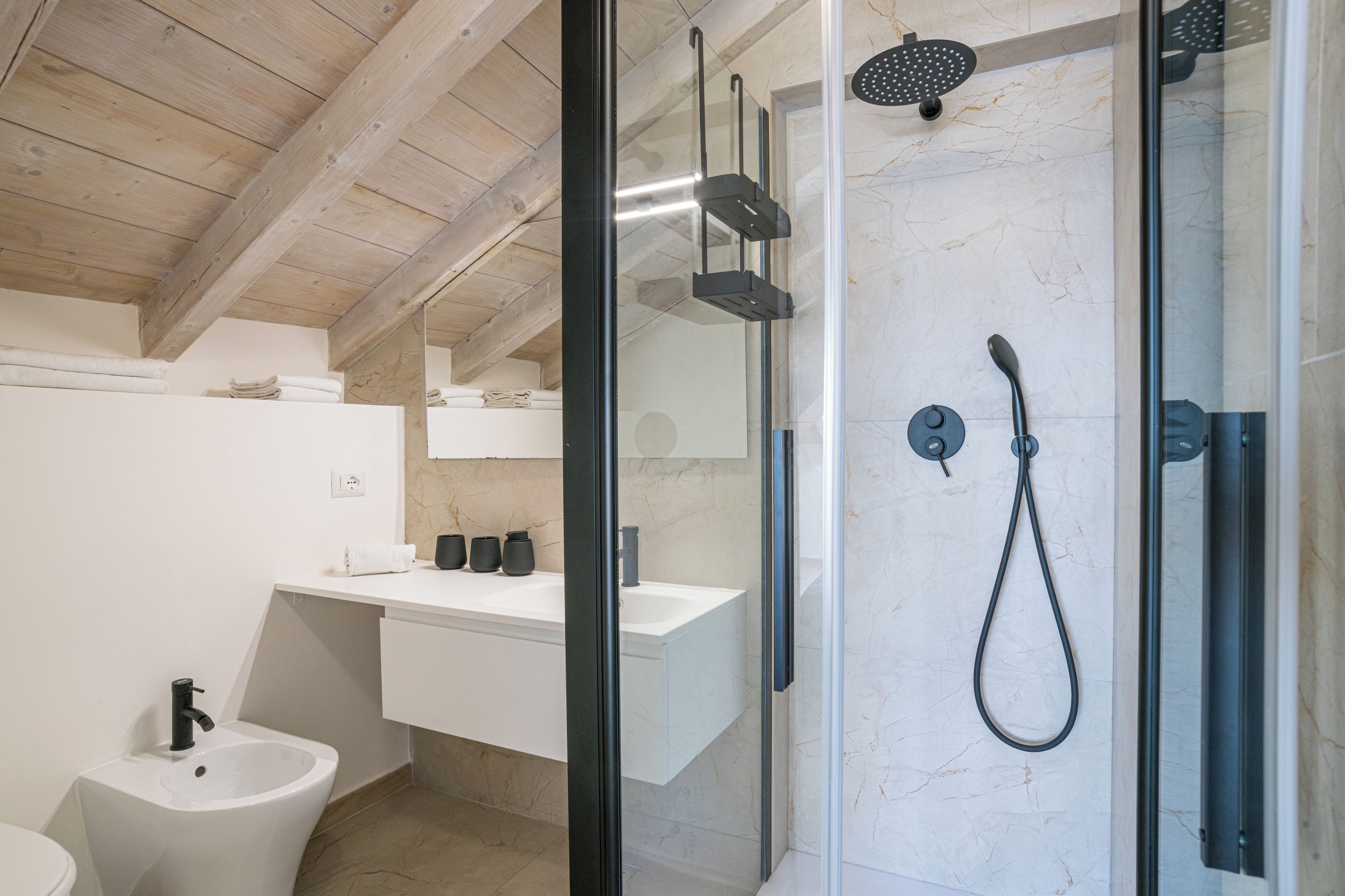 A modern bathroom with a glass-enclosed shower, a bidet, and a white vanity.