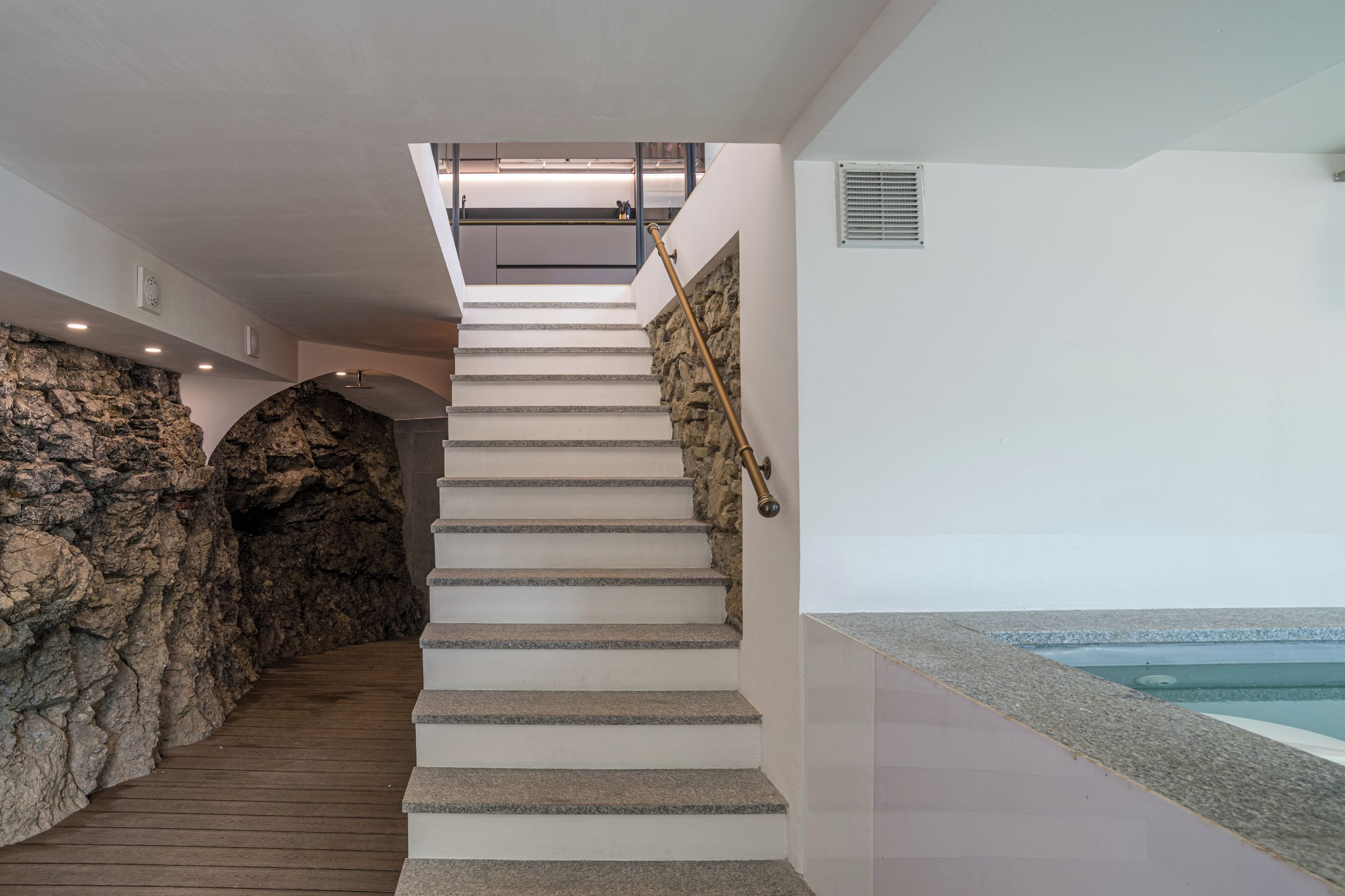 A staircase with stone steps leading to a second floor, a stone wall on the left, and a pool area on the right.
