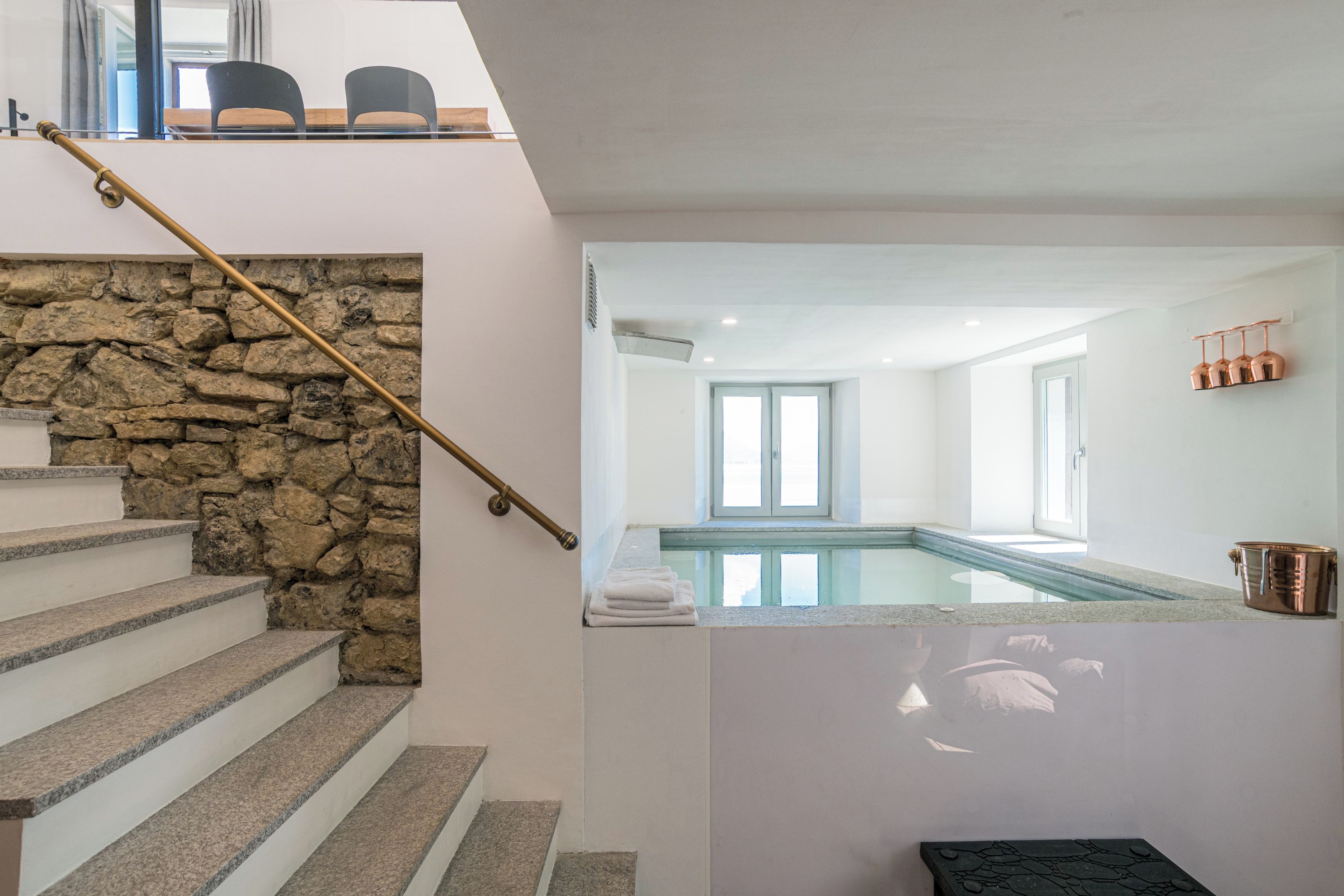 A staircase with a stone wall, a pool area with a glass barrier, and a metal railing.