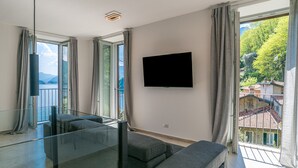 A modern living room with a large window, a flat-screen TV, and a glass railing. - Sant' Anna Deluxe (Menaggio)