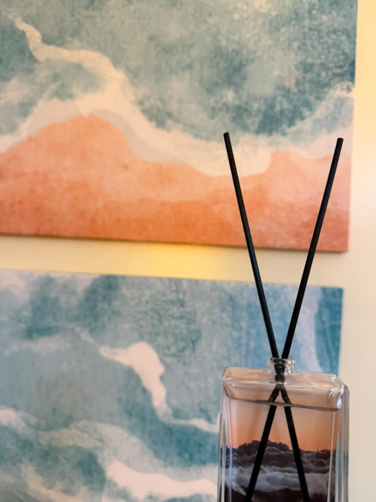 A glass with two black straws and a painting in the background.