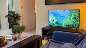 A modern living room with a sofa, a coffee table, a TV, and a painting on the wall. - Trendy 1BR Avida Sucat – Pool & Airport Vicinity (Parañaque)