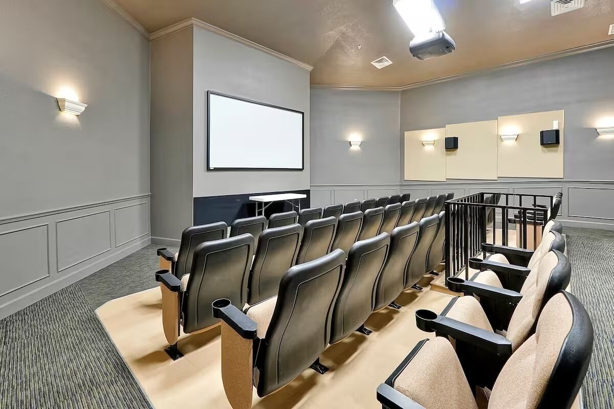 Une salle de cinéma avec des rangées de sièges noirs et beiges, un grand écran et des haut-parleurs fixés aux murs.