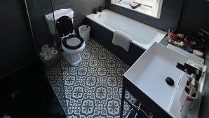 A bathroom with a toilet, bathtub, and sink. There is a window with a view of the outside. - Spacious House in Guildford  (Guildford)