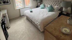 A bedroom with a large bed, a dresser, a radiator, a window with a view, and framed pictures on the wall. - Spacious House in Guildford  (Guildford)