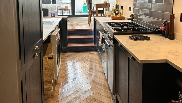 A modern kitchen with dark cabinetry, a central island, and a view to a balcony. - Spacious House in Guildford  (Guildford)