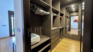 Un dressing accessible sans porte, avec des étagères en bois, un lit recouvert d’une couette blanche et un plancher en bois.