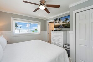 A bedroom with a bed, a ceiling fan, a window with blinds, a dresser, and a door. - Seagrass Sunsets Unit 4 (Bradenton Beach)