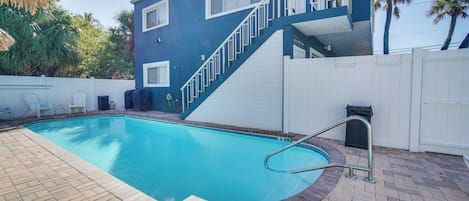 Une piscine dont le bord est recouvert de carreaux bleus, une clôture blanche et un escalier menant à un balcon.