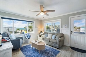 Un salon doté d’un ventilateur de plafond, d’un canapé, d’une table basse et offrant une vue sur l’océan grâce à de grandes fenêtres.