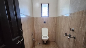 Une petite salle de bain étroite, comprenant des toilettes, une fenêtre et un espace douche.